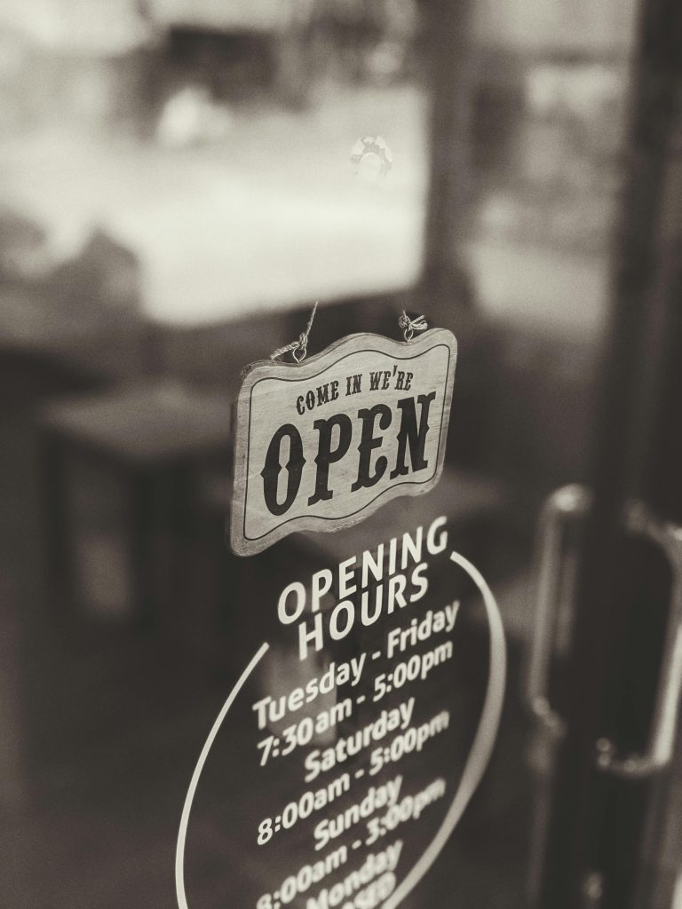 A classic 'Come in, we're open' sign on a glass door in a Bali café with opening hours displayed.