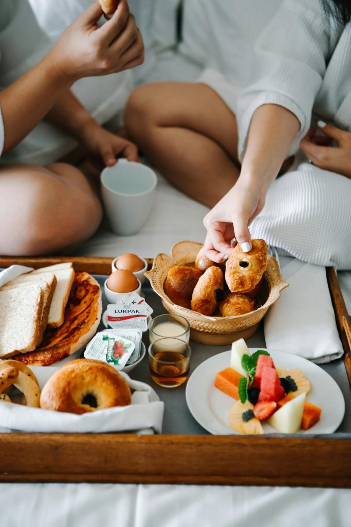 Relaxing morning in bed with coffee, assorted pastries, and fresh fruit on a wooden tray.