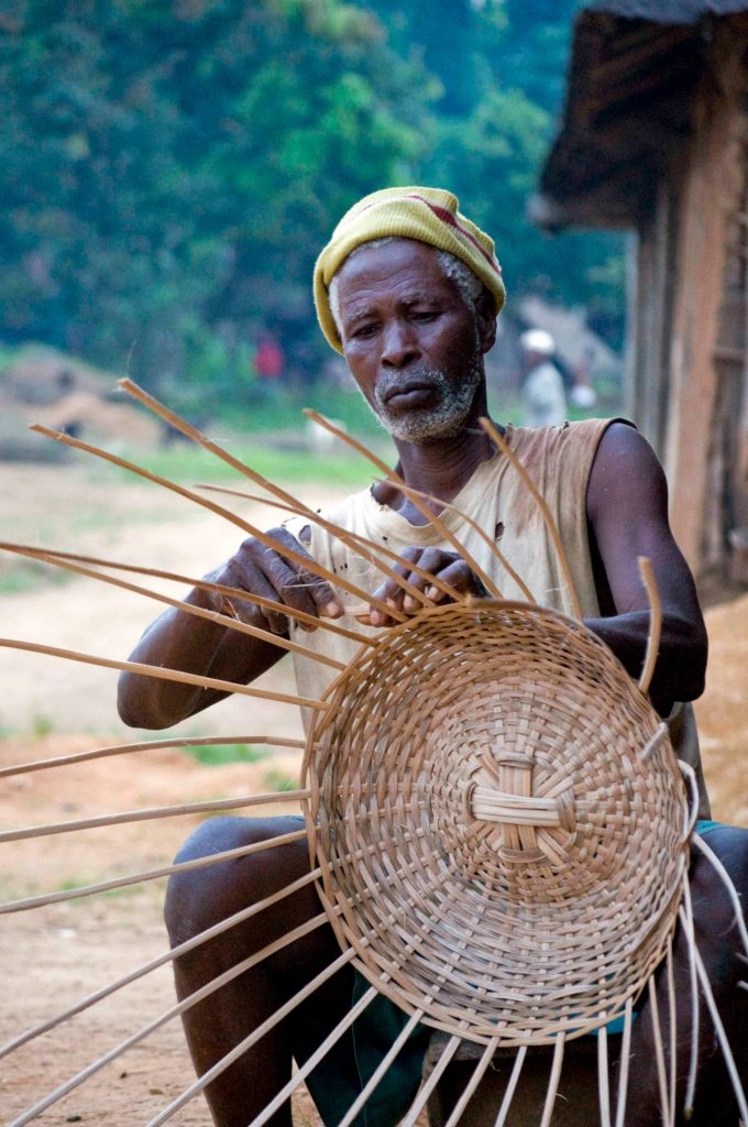A man intricately weaving a basket outdoors in Sierra Leone.