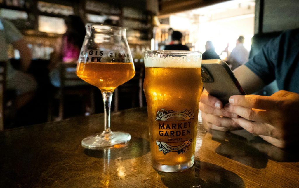 A cozy pub scene showing two beers on a table as someone uses a smartphone.