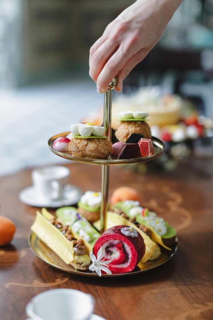 Hand selecting pastries from a refined two-tier dessert stand indoors.
